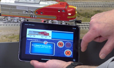 Hands holding a tablet controlling a toy train.