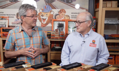 Two men at a table surrounded by toy trains and a toy train display.