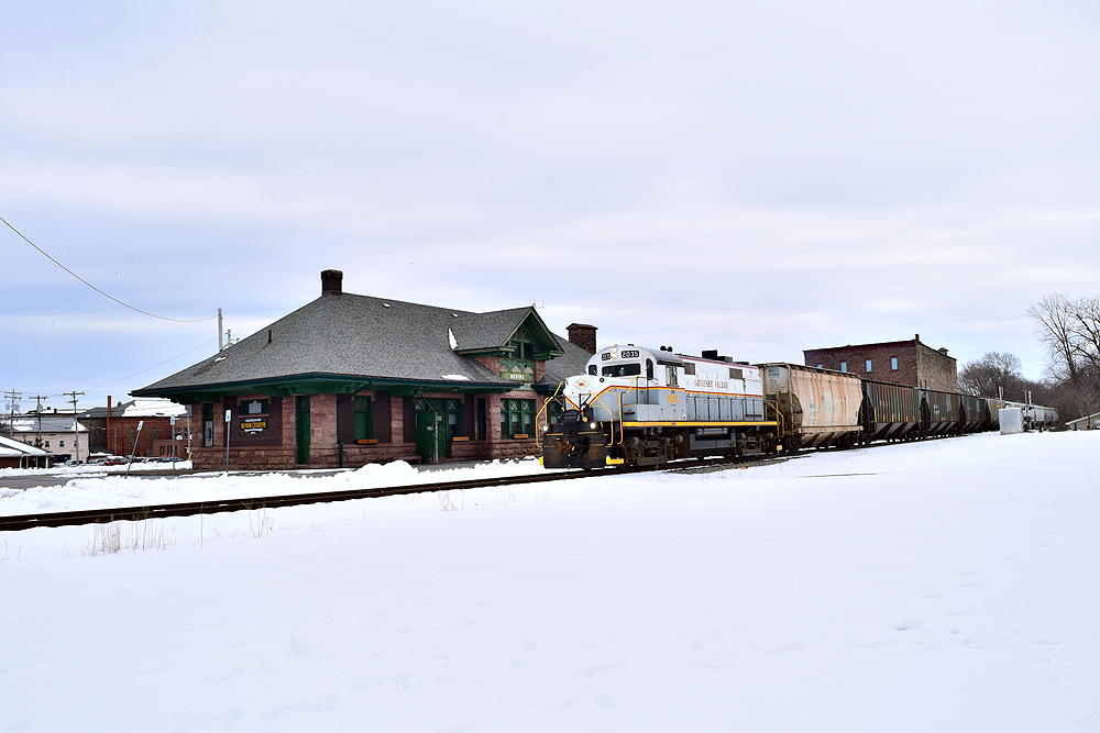 Alco locomotive next to a depot on a snowy day.
