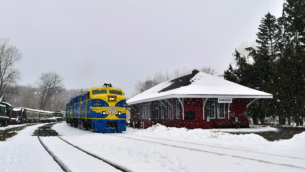 Blue-and-yellow cab unit locomotive next to a depot in a snowy scene.
