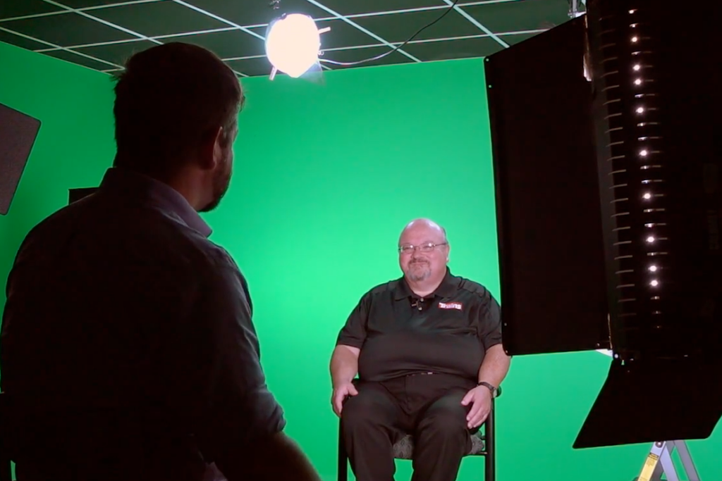 Two men seated in a video studio with dramatic lighting.