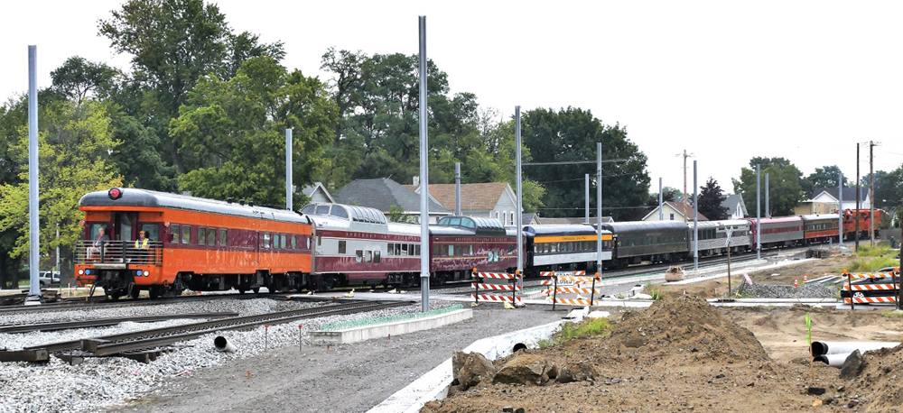 Train of mismatched passenger cars on track surrounded by construction
