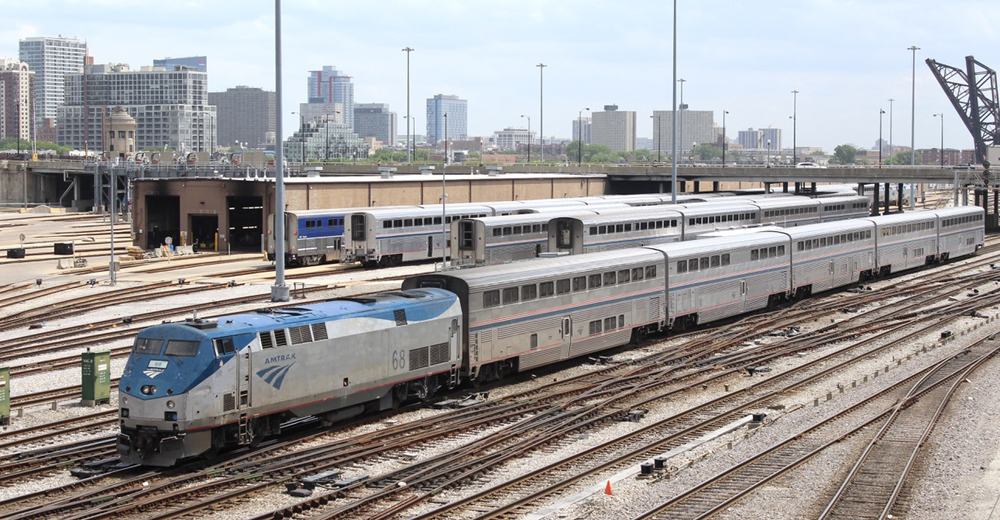 Passenger train with locomotive and five cars passes yard full of passenger equipment