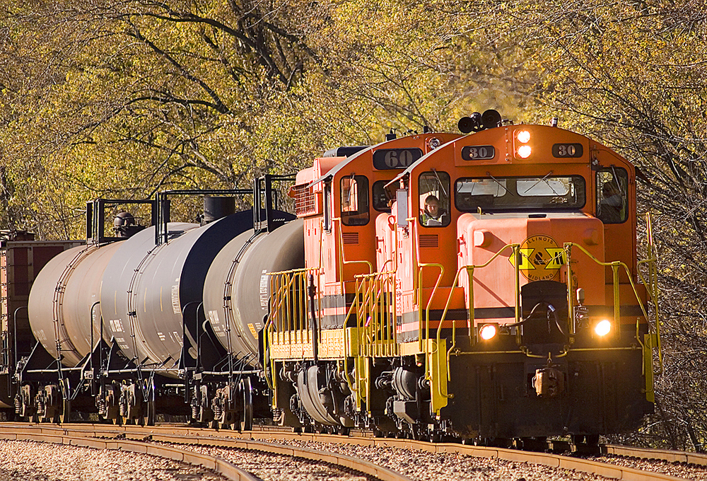 Two orange and black locomotives hauling tank cars