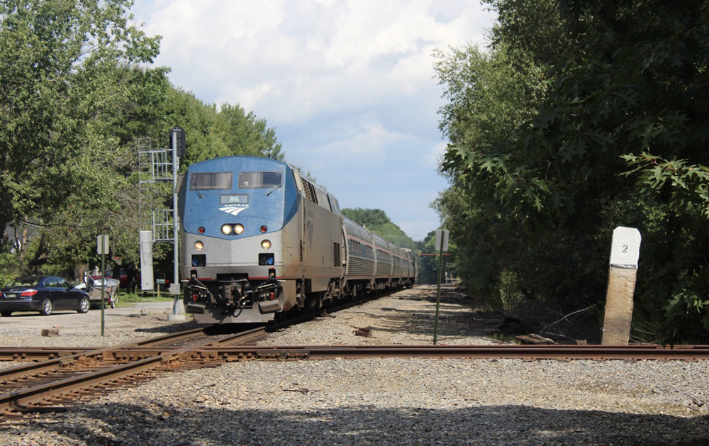 Passenger train crosses diamond in area surrounded by trees