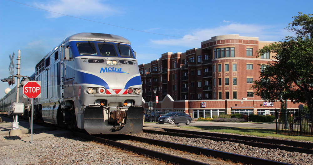 Commuter train passes though town with multistory apartment building next to tracks