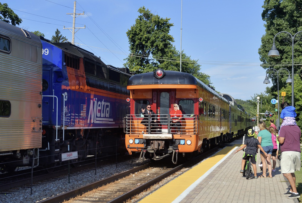 Passenger car with observation platform meets commuter train at station