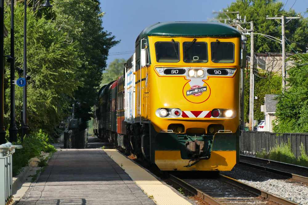 Yellow and green locomotive leads passenger cars through commuter station