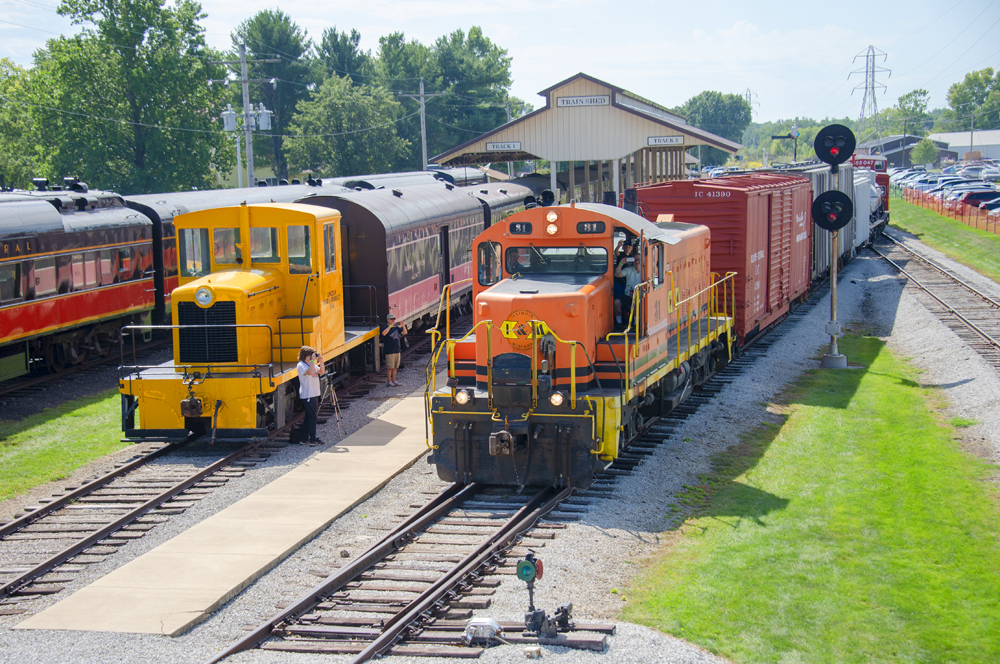 Orange and black locomotive with freight cars passes other equipment