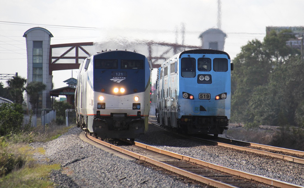 Passenger train meets commuter train with station in background