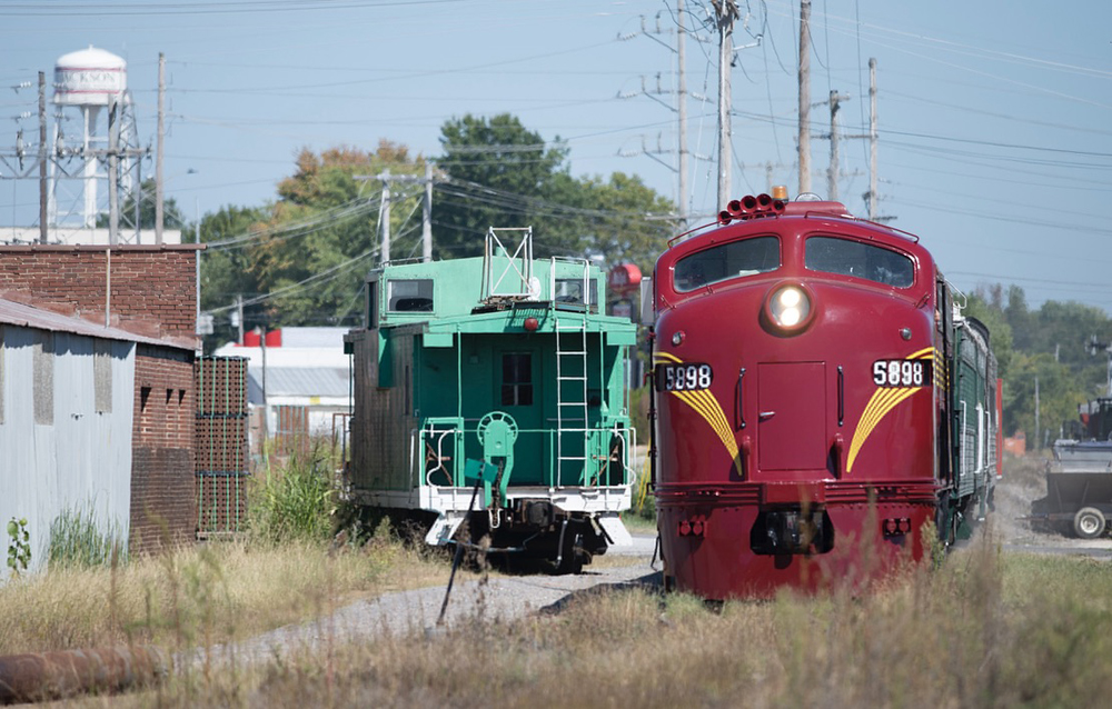 Passenger train with maroon locomotive passes green caboose