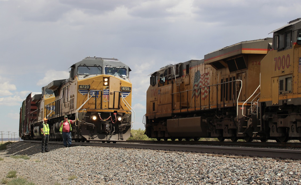 Two men standing by train watch as another train goes by