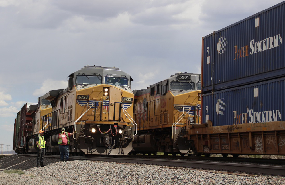 Two crew members stand next to their train as another train passes