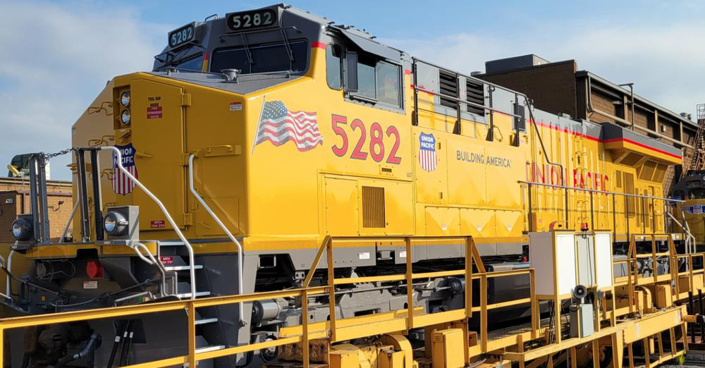 Three-quarter view of yellow locomotive showing American flag decal near nose