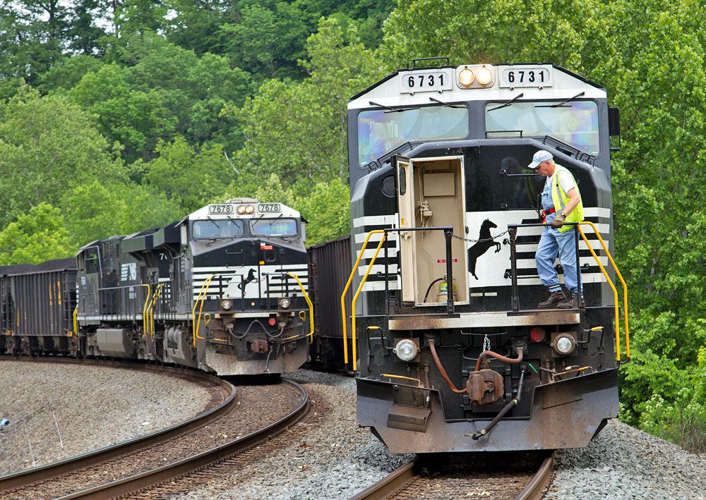 Crew member walks across front of locomotive as another train passes on adjacent track