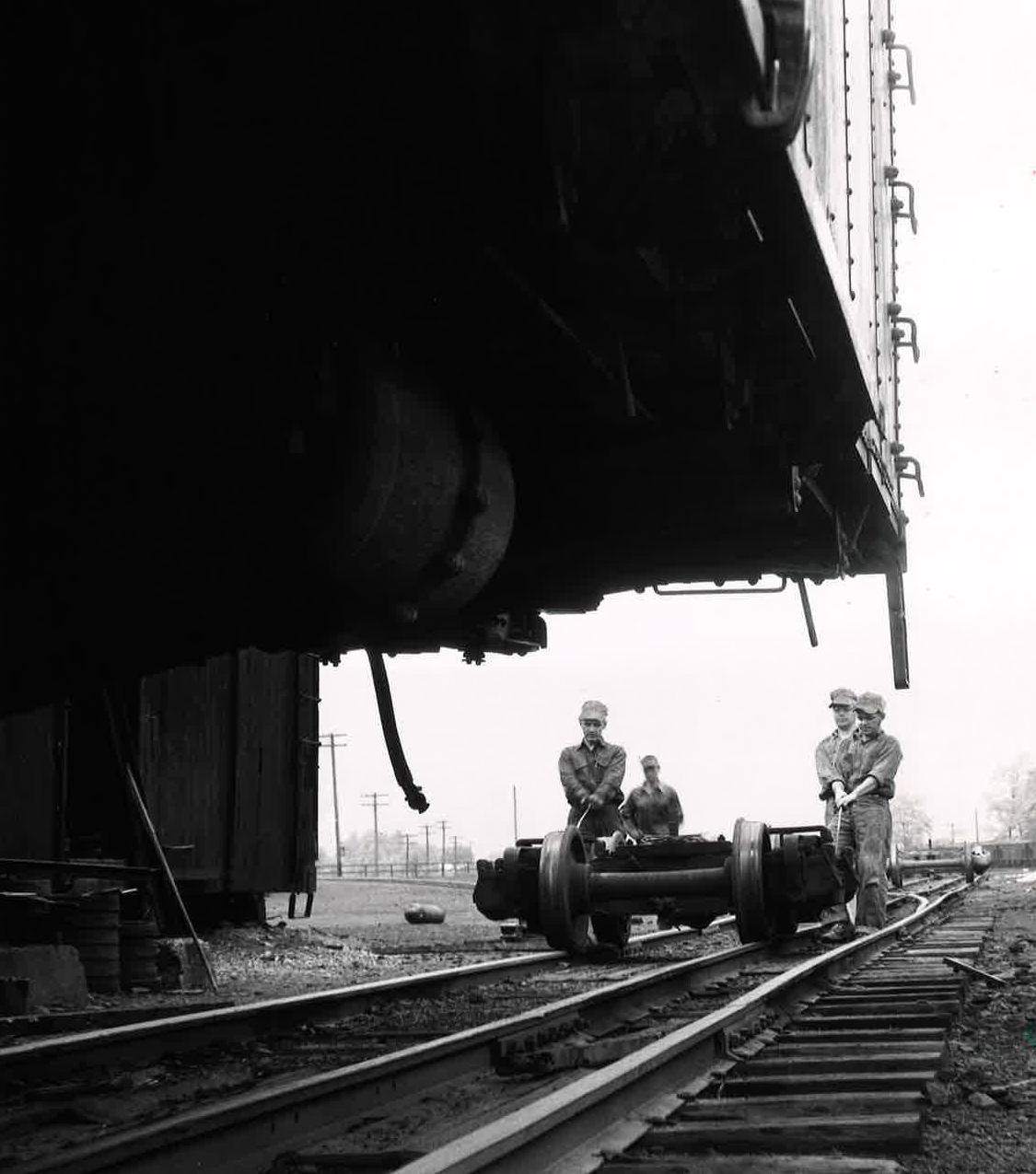 four men roll narrow-gauge truck under boxcar on East Broad Top Railroad
