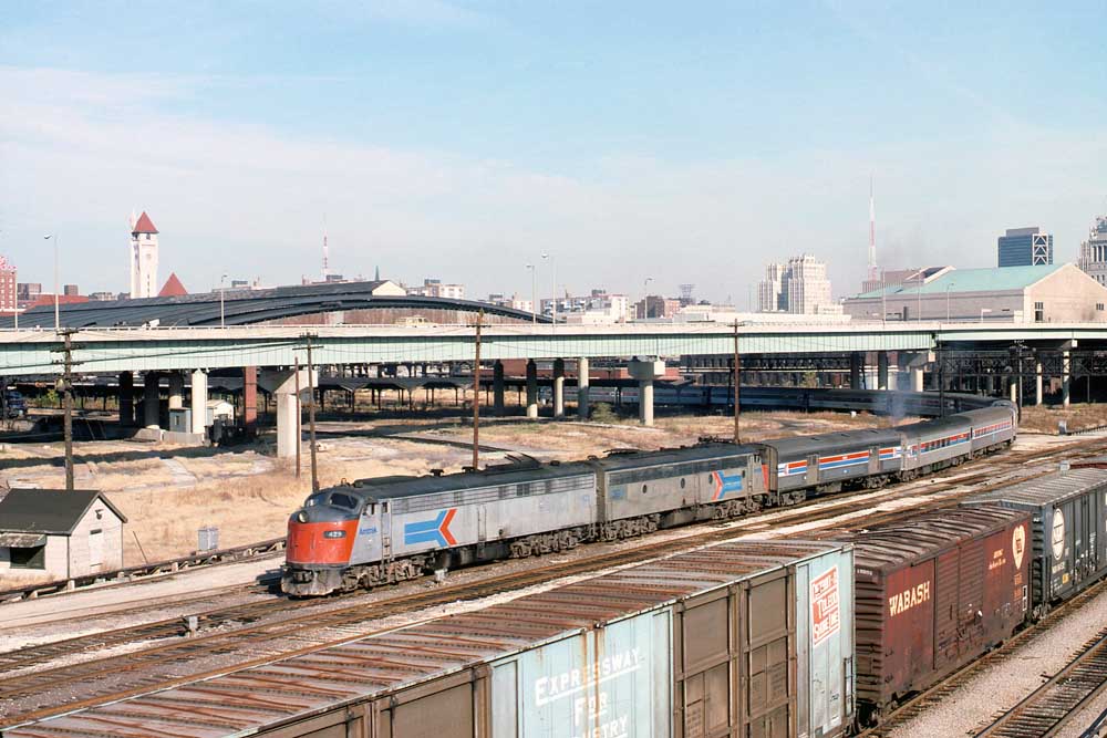 Passenger train between line of boxcars and highway overpass