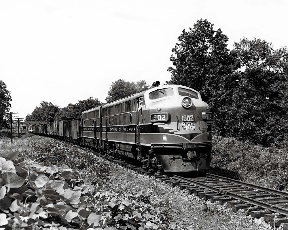 Streamlined Central of Georgia Railway diesel locomotives with freight train in vine-covered countryside