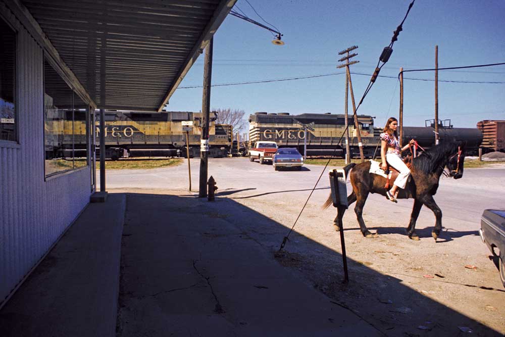 Woman on horse passes in front of freight train