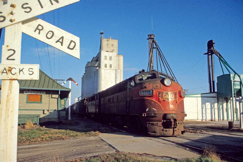 Streamlined diesel locomotive on freight train in town with concrete grain silos
