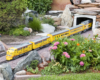 yellow diesel model locomotive emerges from a tunnel on garden railway