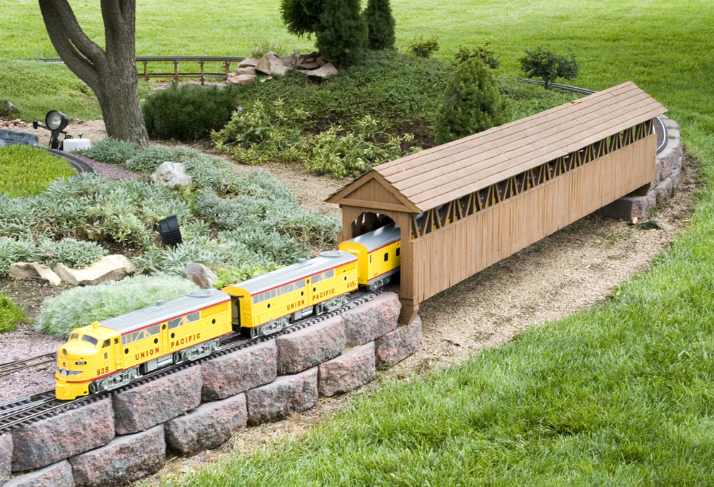 model yellow train exiting covered bridge
