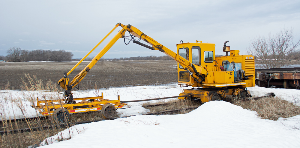 Photo of tie crane and cart parked on siding in partially snow-covered landscape