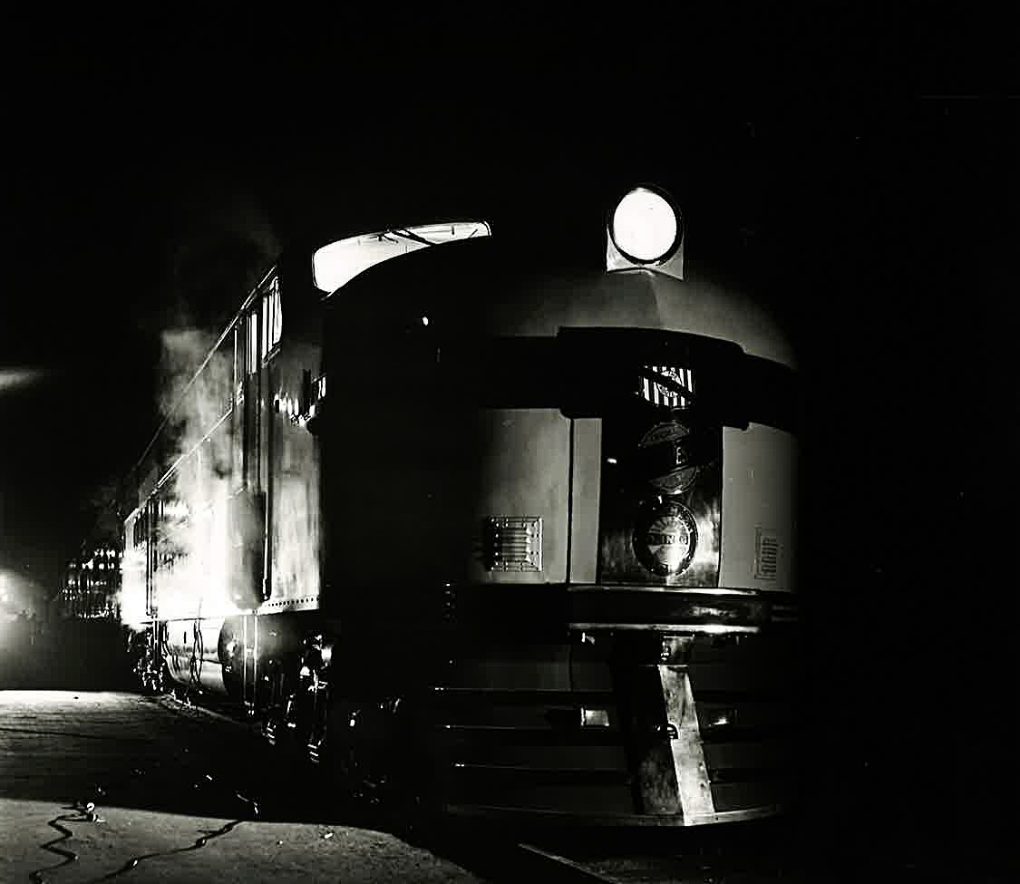 EMD E2 locomotive in dark shadow at station with City of San Francisco passenger train
