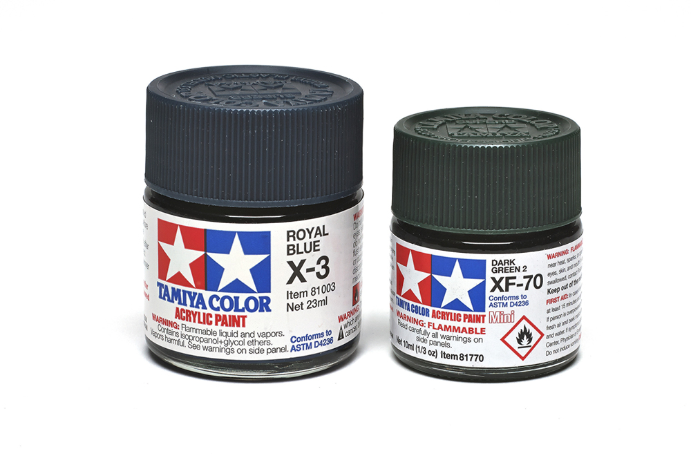 A regular bottle of Tamiya “Royal Blue” and a mini bottle of “Dark Green 2” sit next to each other in front of a white background