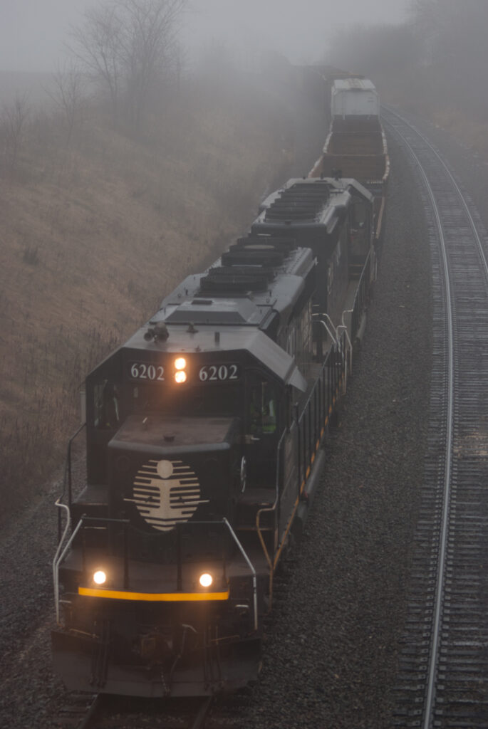 A black painted locomotive leads a train uphill in heavy fog.