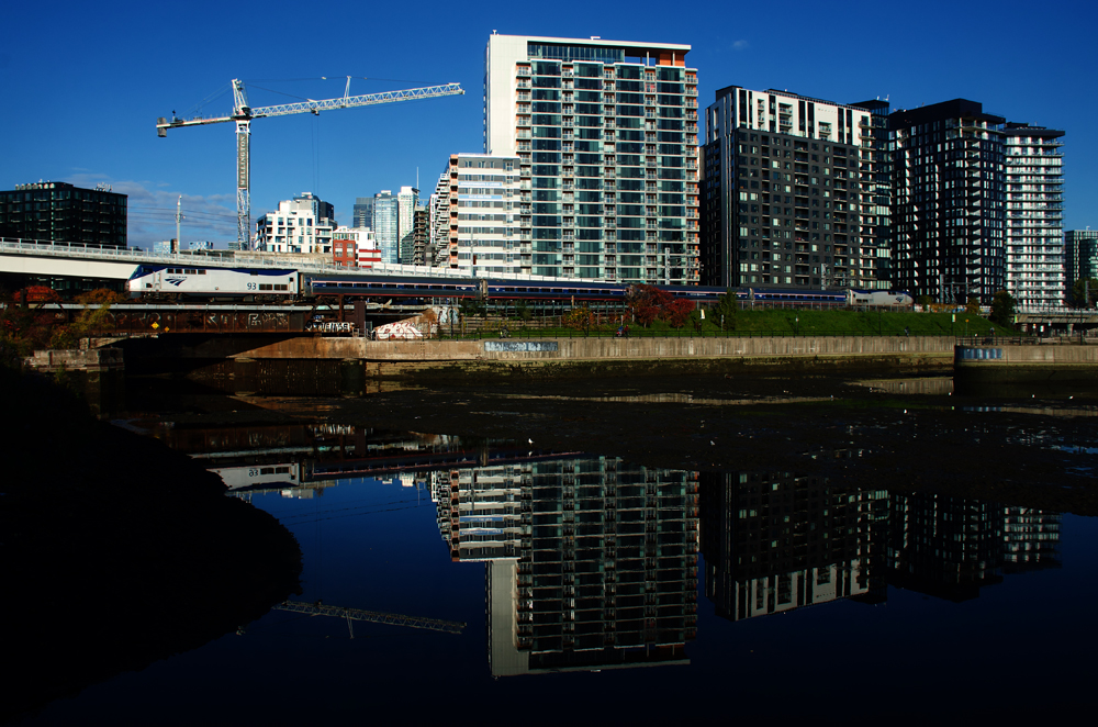 Passenger train on bridge near water, with high-rise apartments in background