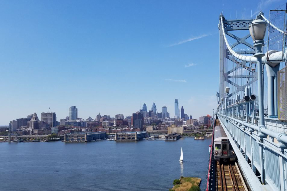 View from side of bridge with rapid-transit train below and Philadelphia in distance