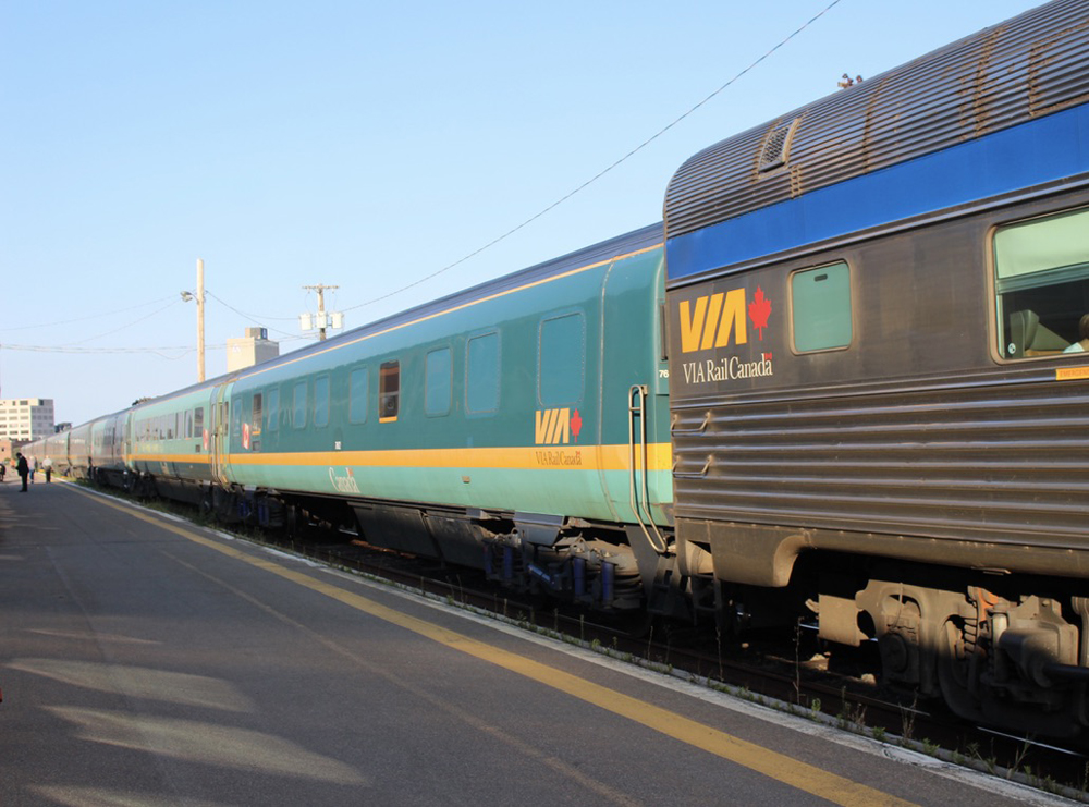 Small smooth-sided two-tone green passenger car coupled to larger stainless steel passenger car