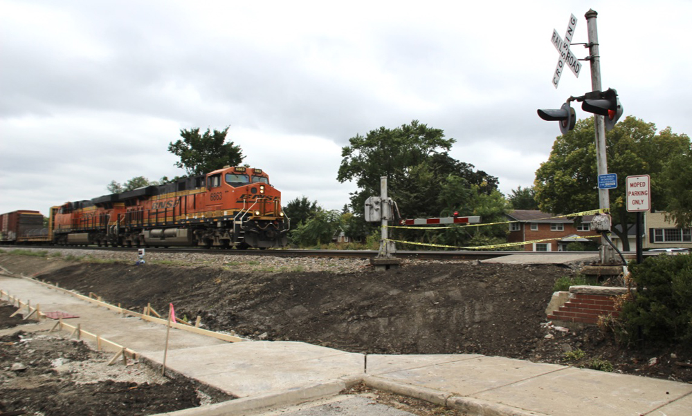 Freight train with orange locomotives approaches crossing gates at closed pedestrian crossing