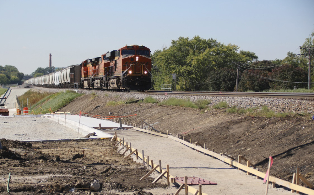Train approaching on straight track with sidewalk construction in foreground