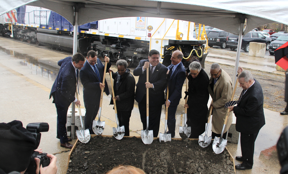 Eight people with shovels digging into box of dirt