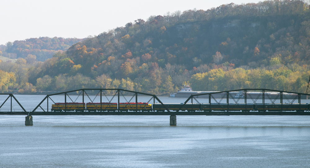 Side view of train crossing bridge over river with fall colors in background
