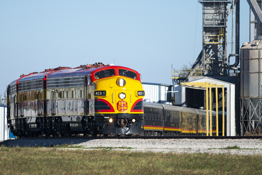 Red, yellow, and black passenger train on loop at grain elevator