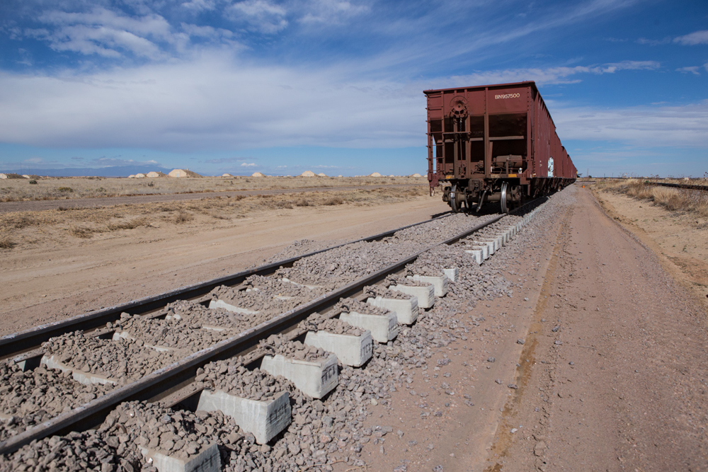 Fresh ballast on track with concrete ties and ballast train in background
