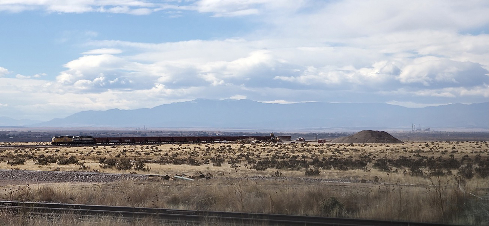 View across plains to ballast train with mountains and clouds in distance