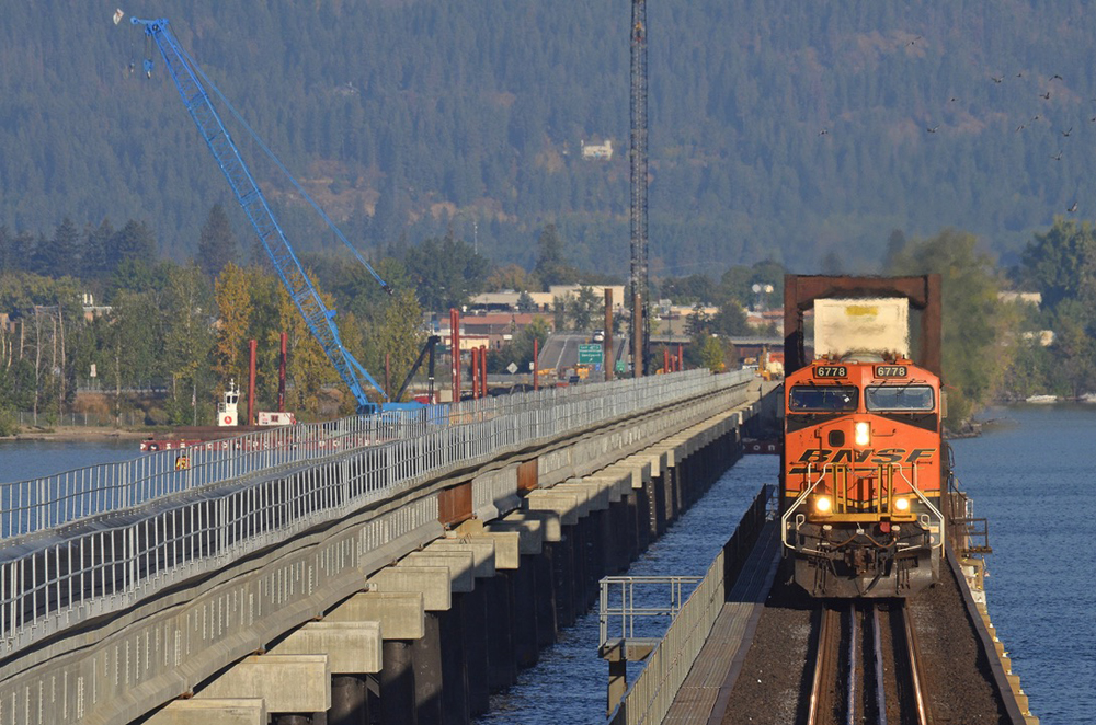 Front view of train crossing bridge with second bridge under construction at left