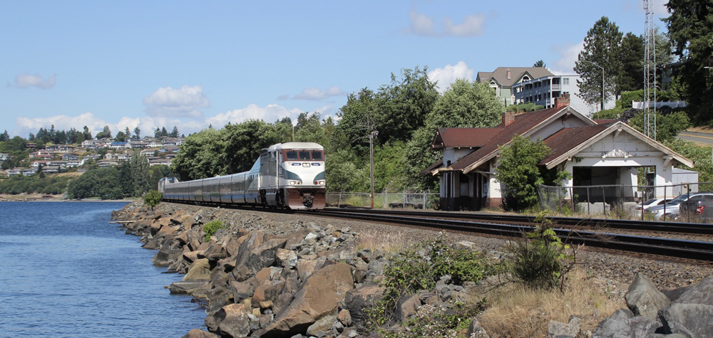 Passenger train on tracks along water, passing closed station