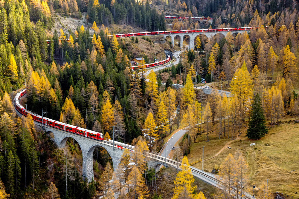 Very long red passenger train winding through mountains