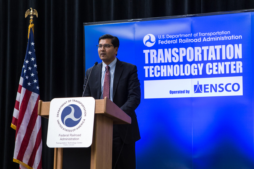 Man at podium with blue "Transportation Technology Center" backdrop