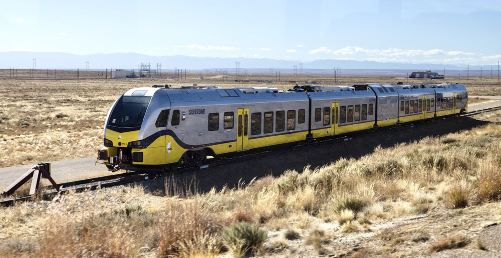 Silver and yellow diesel multiple unit on track surrounded by scrub brush