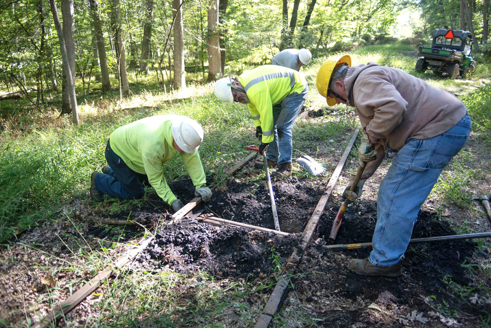 Three people working to nudge rails back into proper gauge