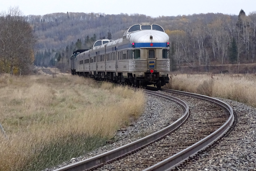 Passenger train with dome-lounge-observation at rear draws away from photographer's location on curve