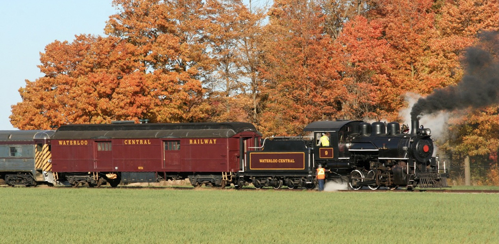 Steam locomotive and passenger cars in front of trees with dramatic fall colors