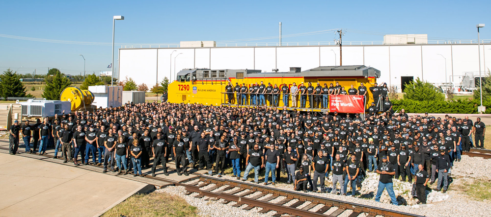 Many people in black shirts gathered around locomotive outside factory