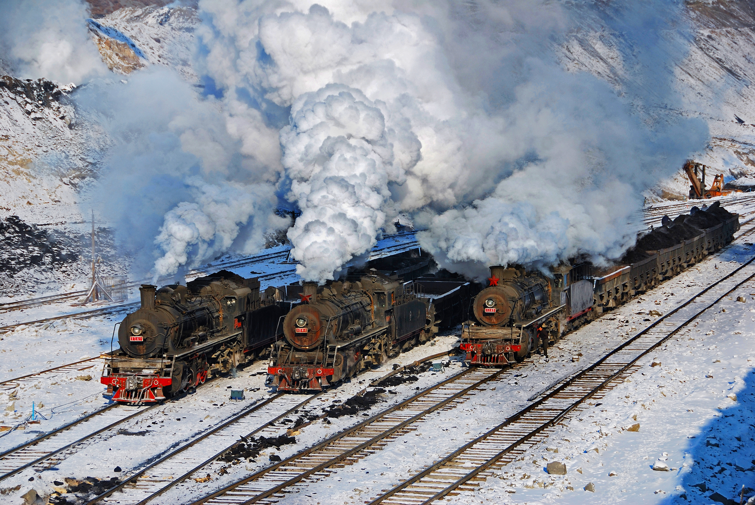 Three steam locomotives next to each other in the snow